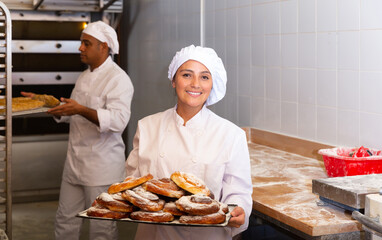 Female baker holding tray of hot sweet pastry in the kitchen of ..bakery