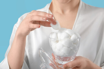 Beautiful young woman with cotton wool on color background, closeup
