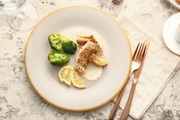 Plate with baked cod fillet, sauce and broccoli on grunge background