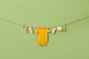 Stylish baby clothes, shoes and accessories hanging on rope against color background