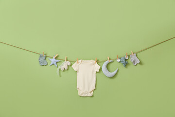 Stylish baby clothes and toys hanging on rope against green background