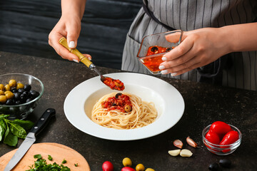 Woman preparing Pasta Puttanesca at kitchen table, closeup