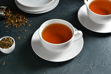 Cups of tasty hojicha green tea on black background