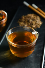 Glass cup of tasty hojicha green tea on black background