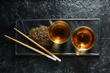 Glass cups of tasty hojicha green tea on black background