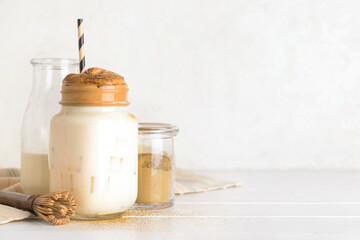 Mason jar of tasty dalgona hojicha latte, chasen and powder on light background
