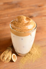 Glass of tasty dalgona hojicha, chasen and powder on wooden background