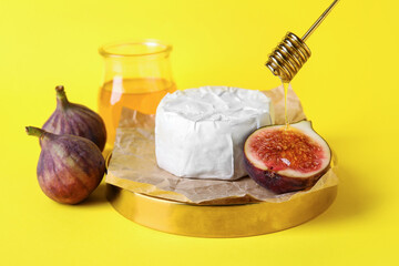 Board with cheese, fresh ripe figs and honey on yellow background