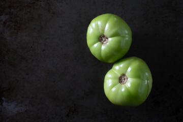 Two green tomatoes, plump and waiting to be sliced for frying.