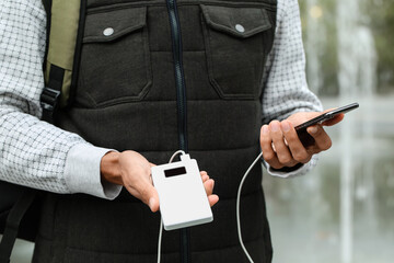Young man with phone and power bank outdoors, closeup