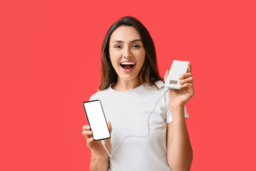 Young woman with phone and power bank on color background