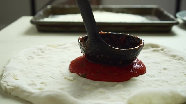 Close up of Chef while spreading Tomato Sauce on Pizza Dough with a Ladle in Traditional Italian Pizza's Restaurant. Italian Food. Pizza's Making.
