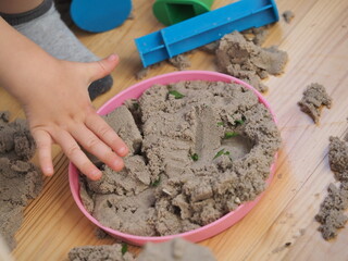 the hands of a toddler playing with kinetic sand