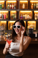 Nightlife concept a sexy girl wearing sunglasses looking mysterious with a straight face holding a drink with cherry on the top
