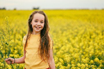 Naklejka na ściany i meble Pretty long haired girl playing in vibrant canola field in full bloom