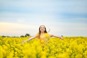 Pretty long haired girl playing in vibrant canola field in full bloom