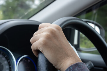 Young woman's hand is holding the black steering wheel of a car.