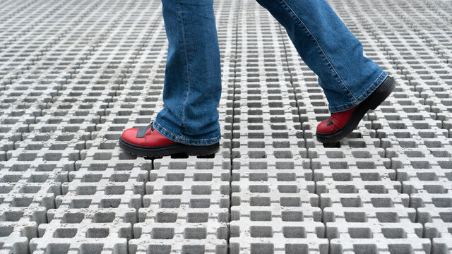 Legs walking on the paving slabs. Feet in red shoes on the road. Cantry red boots walking on pavement. Blue jeans