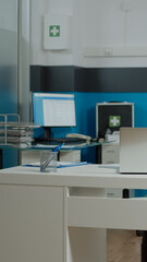 Empty room of medical cabinet at healthcare clinic for patient appointments and health consultations. Nobody in doctors office with laptop, monitor, stethoscope on desk and white bed
