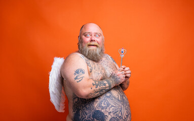 Fat amazed man with beard ,tattoos and wings acts like an magic fairy