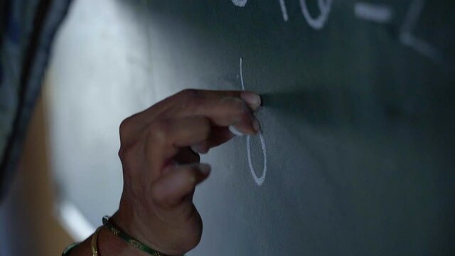 Indian tribal village female teacher writing on blackboard or chalkboard.