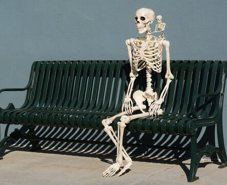 Skeleton sitting on bench with small skeleton on shoulder as a symbol of conscience monitoring internal thoughts
