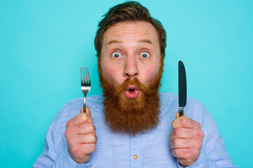 Shocked man with tattoos is ready to eat something with cutlery in hand