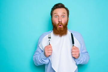 Shocked man with tattoos is ready to eat something with cutlery in hand