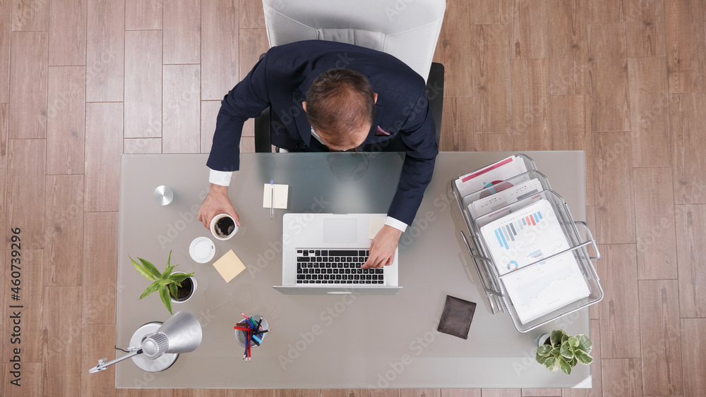 Poster top view of businessman holding cup of coffee while typing company statistics working at management 