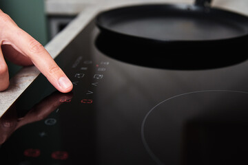 Modern kitchen appliance. Woman hand turn on induction stove to cook. Finger touching sensor button on induction or electrical hob