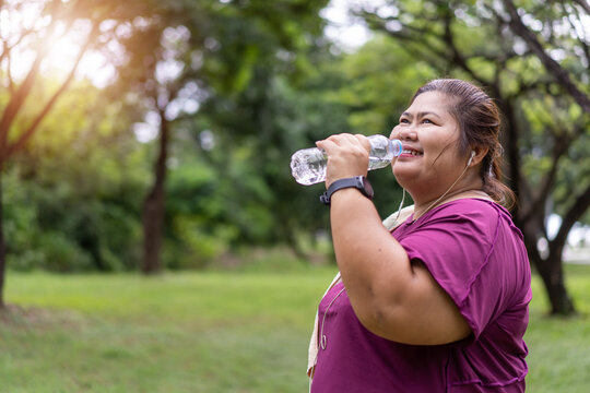 Asian fat woman drinking water bottle with workout outdoors exercising in park, Sport and recreation for weight loss idea concept.
