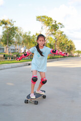 Asian little girl child skateboarder wearing safety and protective equipment playing on skateboard. Kid skateboarding on the road outdoors