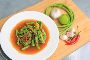 Spicy Long Beans salad in white plate on wooden board against grey marble background