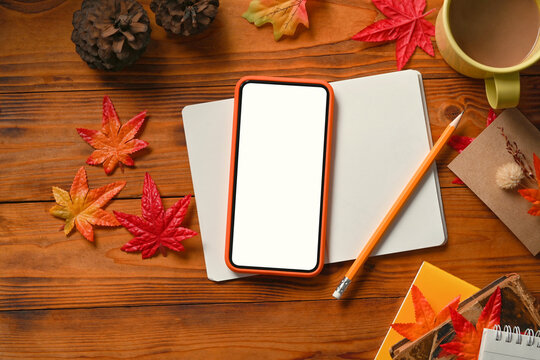 Smart phone, notebook, coffee cup, pine cone and Autumn maple leaves on wooden table.