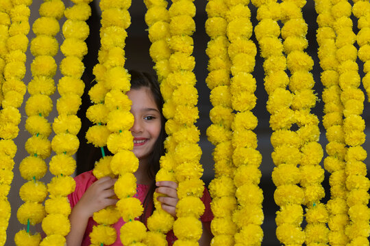 A little girl dressed in traditional wear standing behind festive flower garlands decoration.