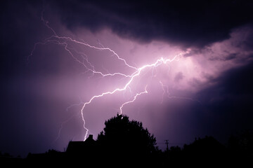 Naklejka na ściany i meble Multiple lightning strikes painting the sky purple on a summer evening during a thunderstorm