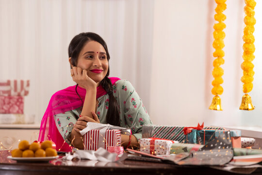 A woman gazing sideways while sitting amidst presents,sweets,Diwali light and festive garland decoration.