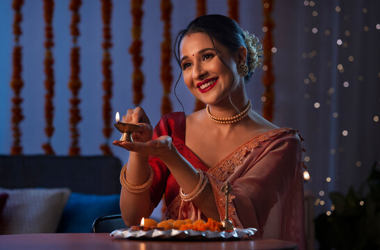 A beautiful woman holding a diya and smiling amidst diwali decoration, lights and a pooja thali.