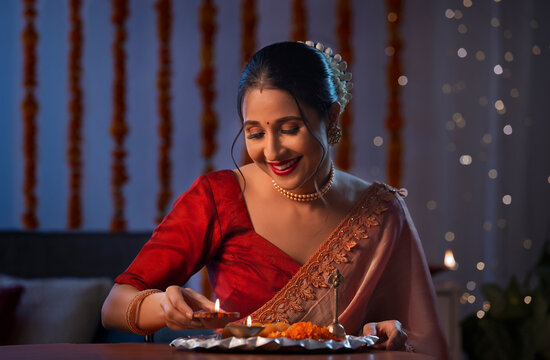 A beautiful woman putting a diya and smiling amidst diwali decoration, lights and a pooja thali.