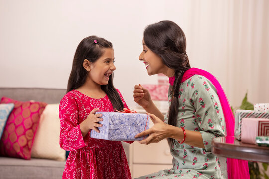 A daughter delighted at gift given by mother amidst other presents kept in room.