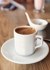 Traditional Turkish coffee in small white cup on wooden table. Selective focus. Vertical photo