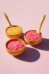 Wooden bowls with a spoon filled with pink and yellow bath sea salt. Beauty treatment for spa and wellness on pink background. Skincare natural cosmetic concept for body care
