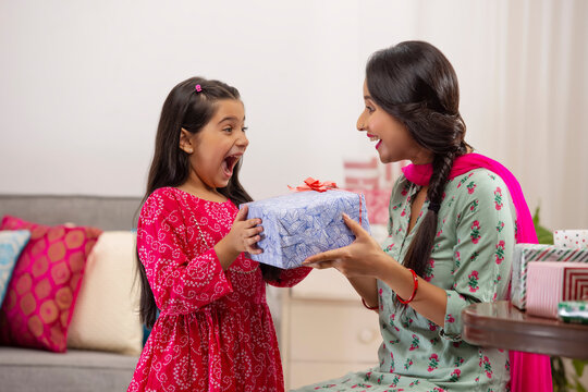 A daughter overjoyed at gift given by mother amidst other presents kept in room.