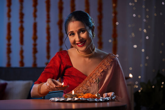 A beautiful woman holding a diya and smiling amidst diwali decoration, lights and a pooja thali.