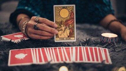 Fortune teller holding THE SUN card and tarot cards. tarot cards and burning candles. Astrologists and forecasting concept.