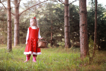 A little girl in a red hat and dresses is walking in the park. Cosplay for the fairytale hero...