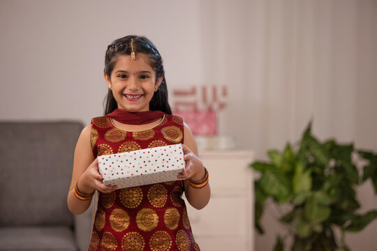 A small girl dressed In traditional cloth happily holding a gift box.