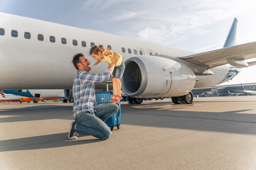 Happy male parent with hid kid near a white plane waiting for a trip. Travel concept