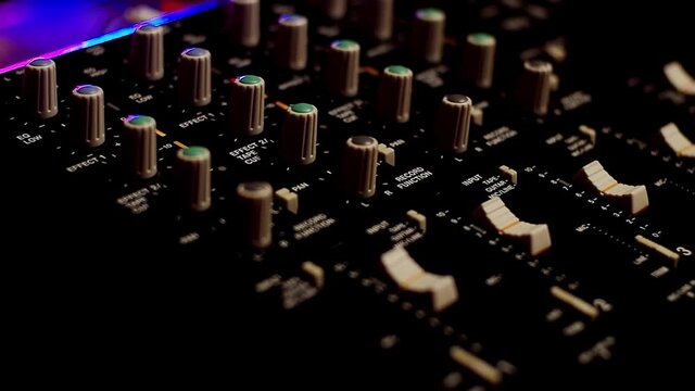 Portative cassette tape studio closeup shot. Hands adjusting mixer knobs. Neon lights.