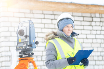 a young female surveyor works with an electronic total station in winter, performing geodetic works...